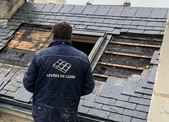 Couvreur des Levées de Loire devant un toit d'ardoise ouvert, liteaux à nu et fenêtre de toit en cours de pose à Mauges-sur-Loire
